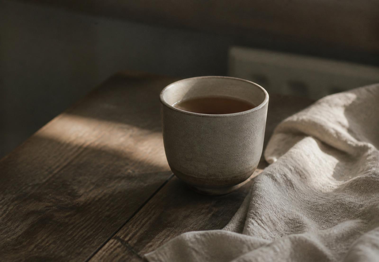 A stoneware cup of tea on a wooden table in soft afternoon light
